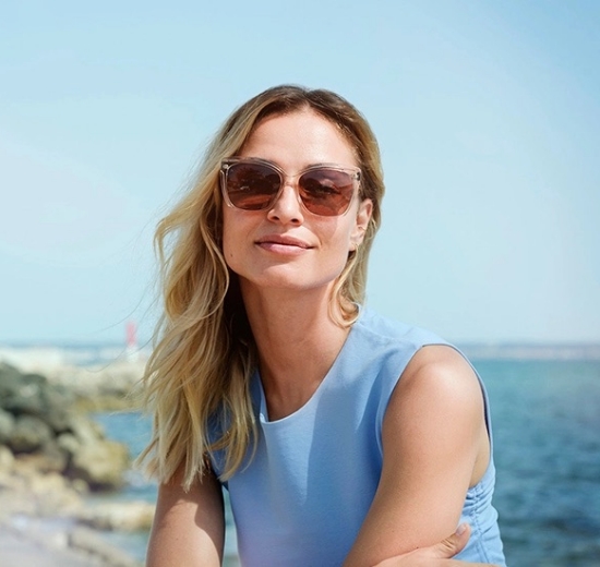 Frau sitzt am Meer mit Sonnenbrille. 